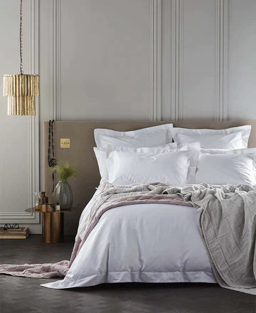 White bedding on a bed with a panelled wall and a pink and grey throw on the bed.