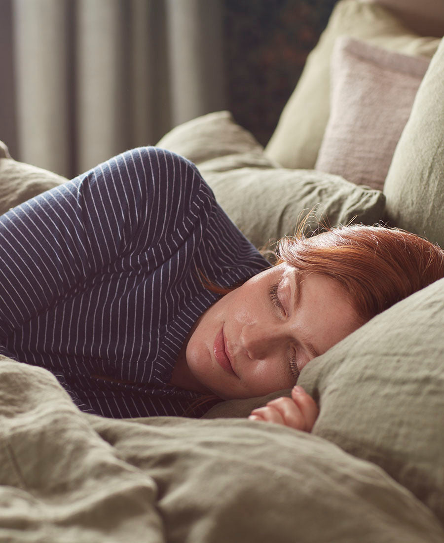 A woman sleeping in a bed with lots of cosy pillows.