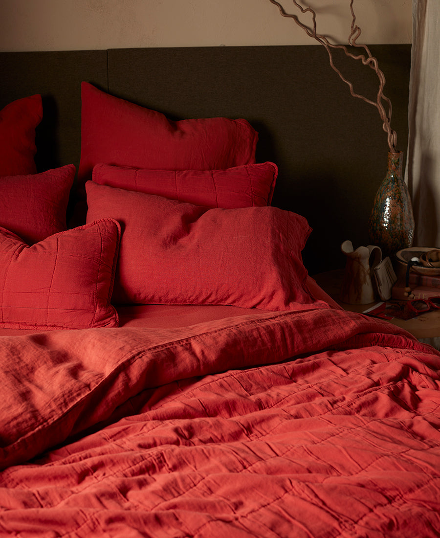 A bed is made up with bright red bedding with cosy throws and pillows.