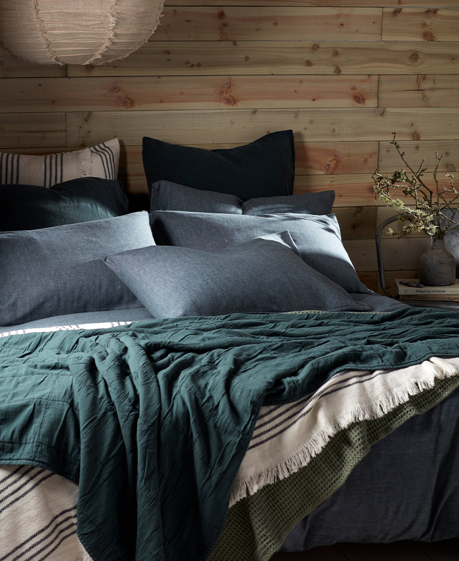 A shot of dark green bed linen with warm white and dark green throws with a panelled wall.