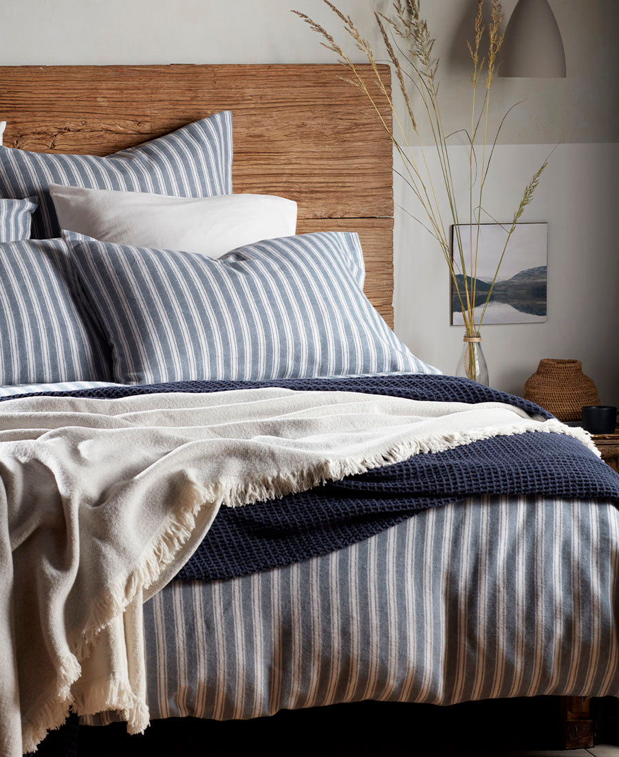A cosy blue and white striped bed with throws and pillows.
