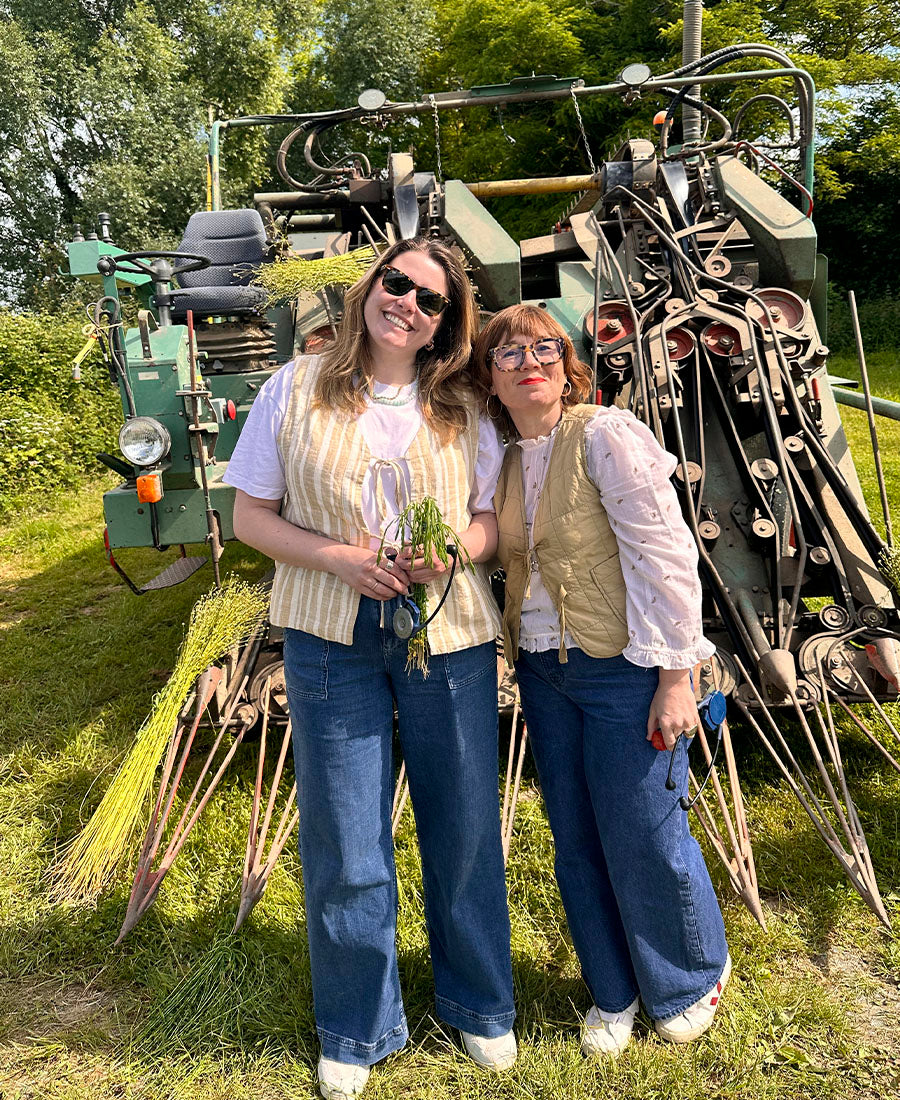 Two women stand in front of flax harvesting machinary.