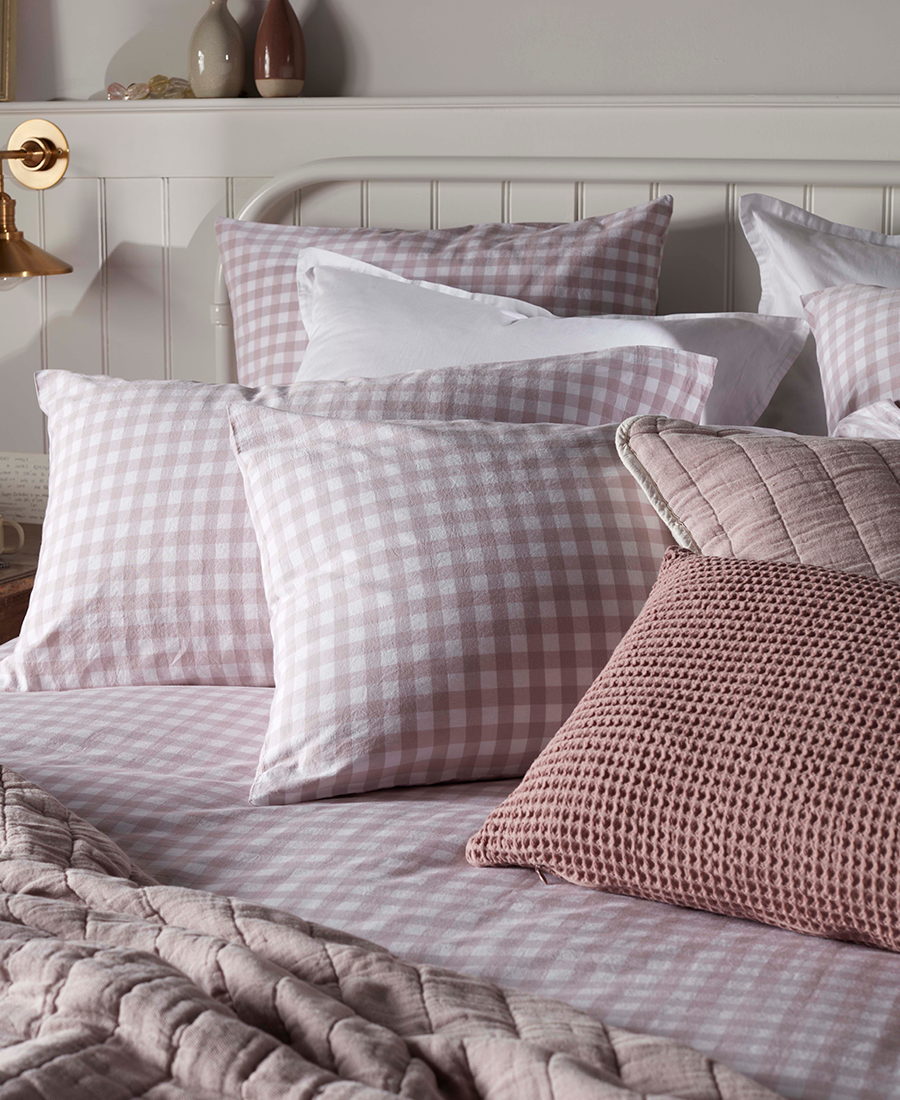 A bed with pink gingham bedding with pink cushions & throws