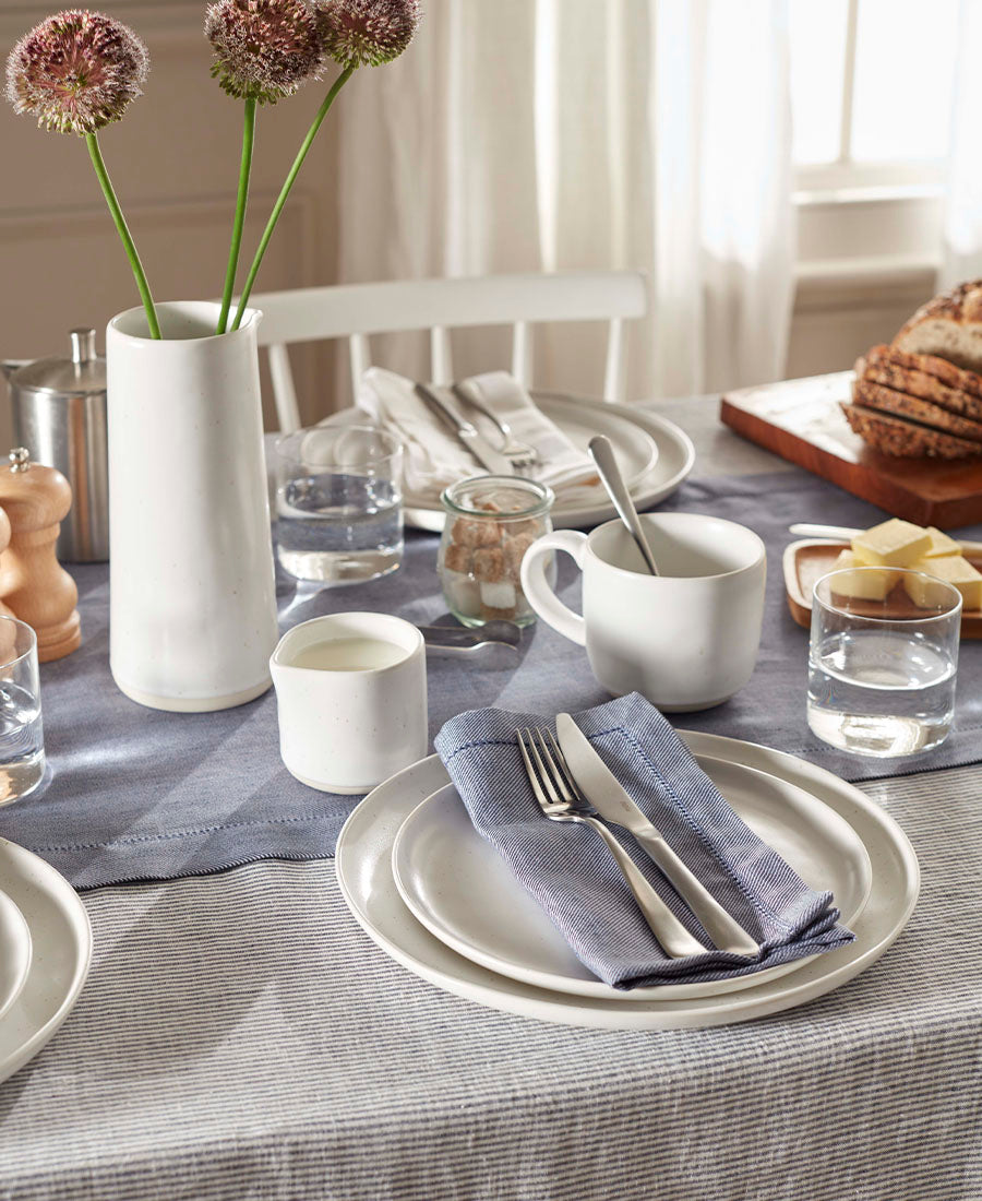 A table is laid for brunch with blue table linen and striped napkins..