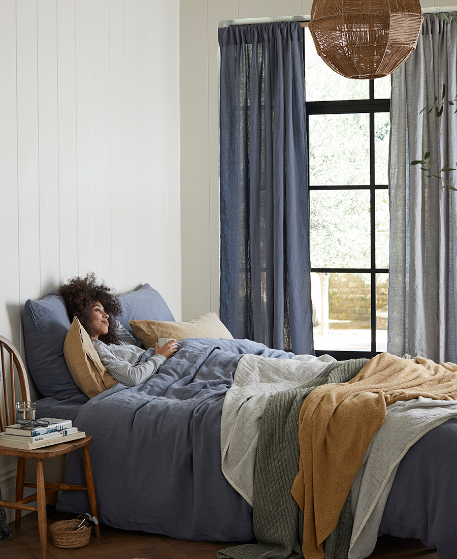 A woman is in bed with cosy throws and cushions.