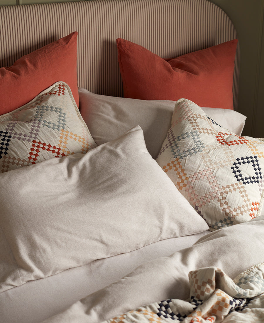 A woman is smiling lying on a bed filled with cosy pillows and throws.