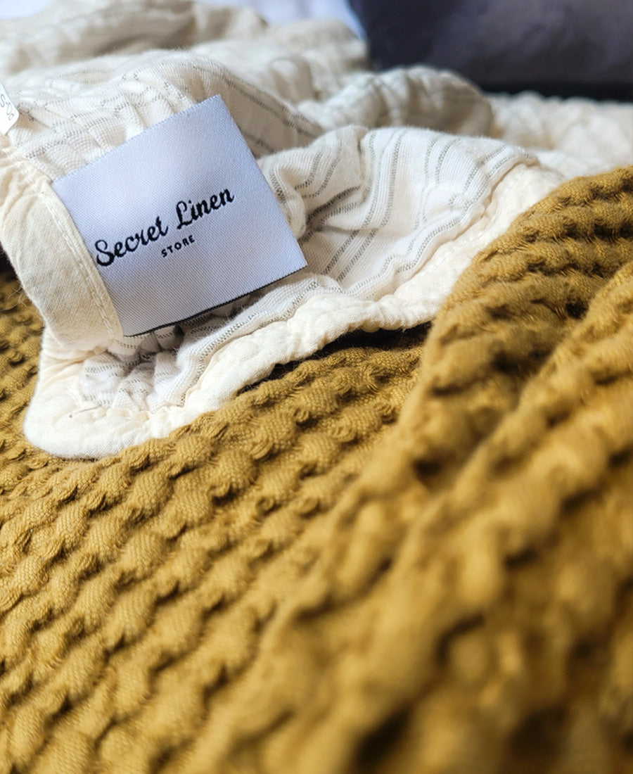 A close up of our  Green Vivienne Throw and Tapenade Wolcutt throw with our Secret Linen Store label.
