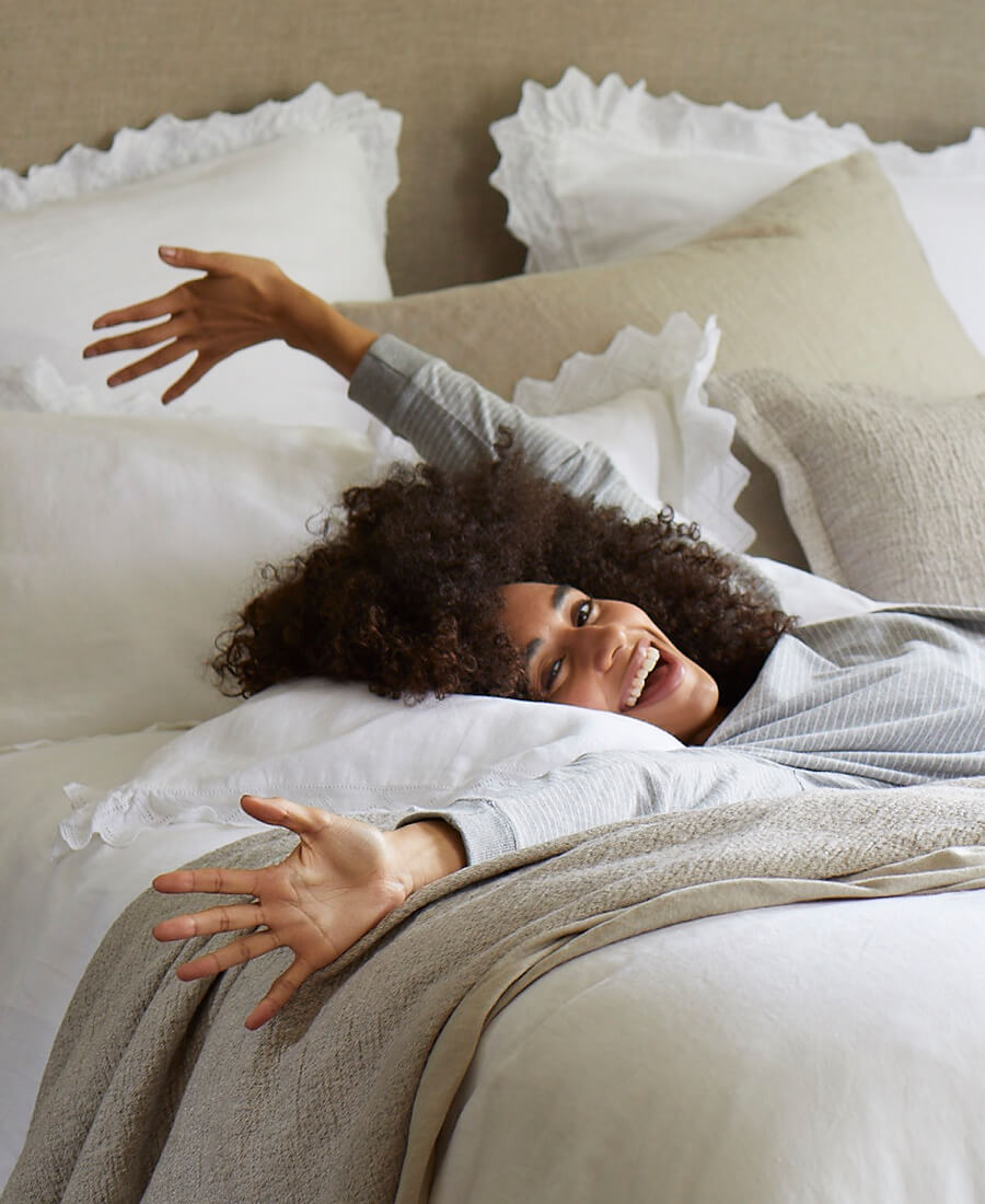A woman is reclining on white and natural bedding