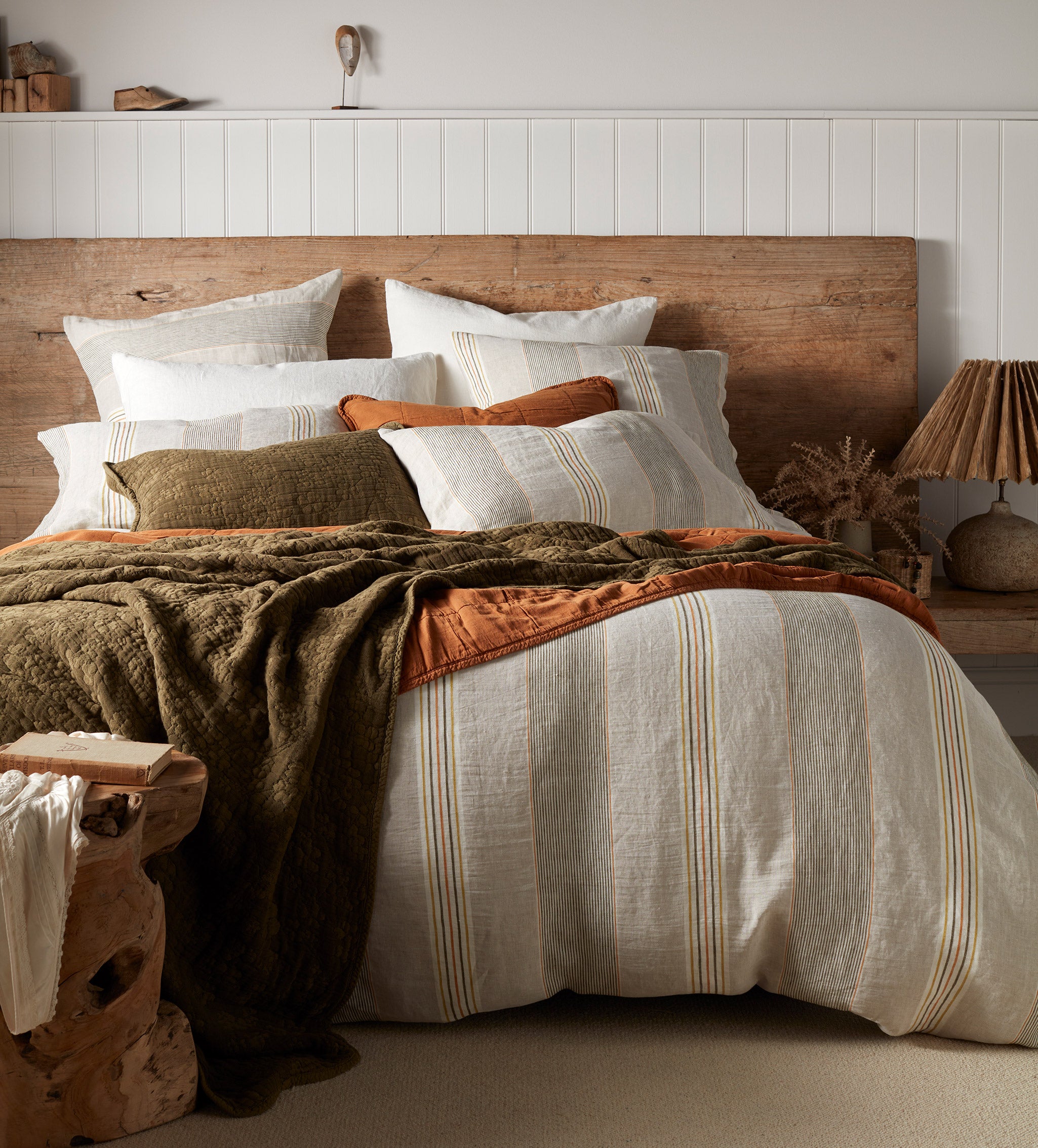 A linen duvet cover with vertical stripes in various shades of green and yellow, displayed on a bed with matching pillowcases and a textured knit throw in a bedroom setting.